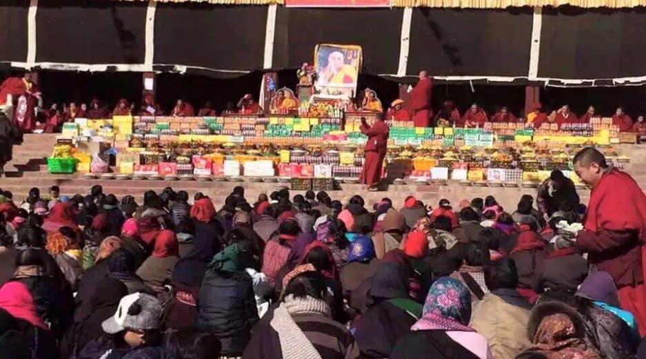 Auf einem Platz beten Menschen vor einem großen Gebäude für die Genesung des Dalai Lama
